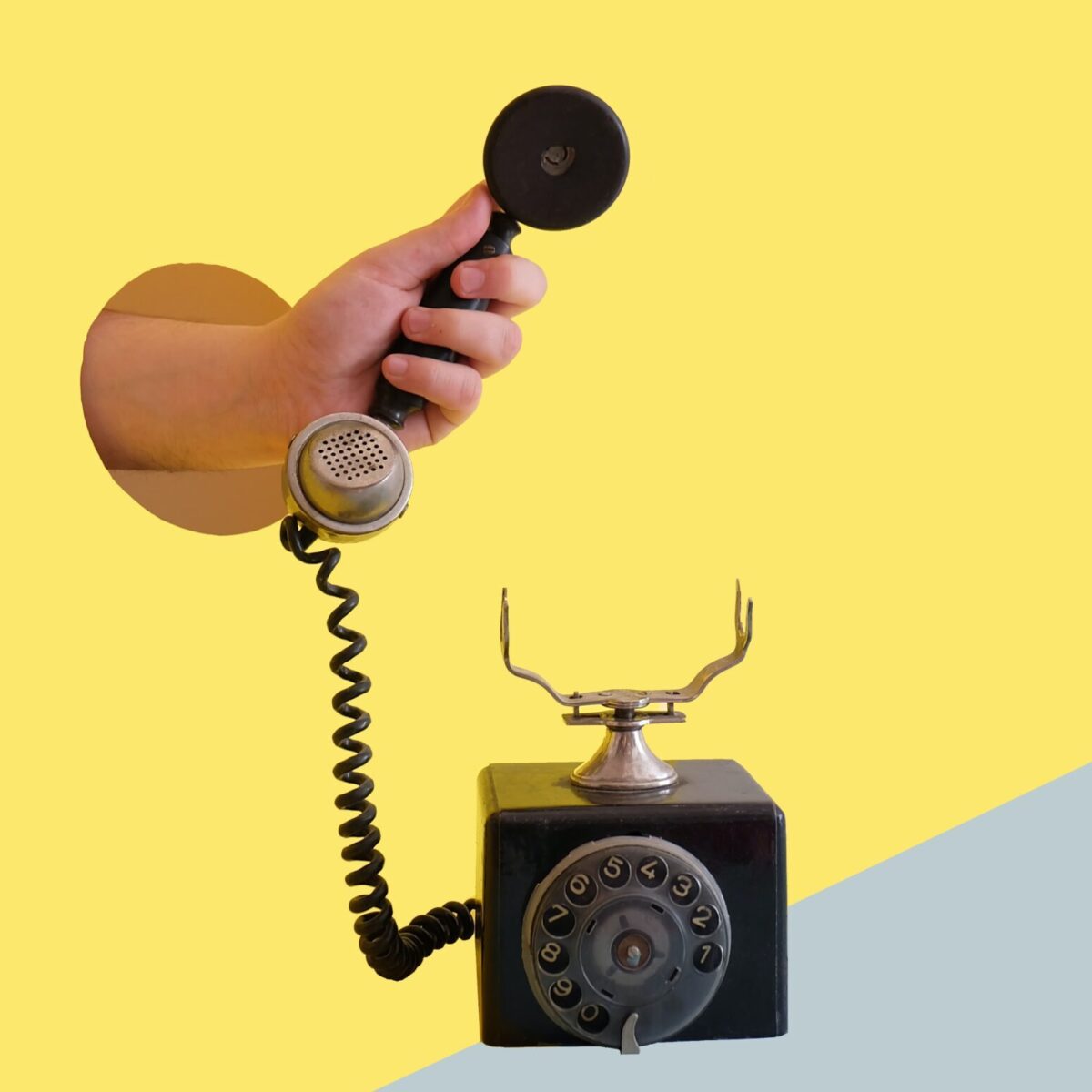 Hand coming out of a hole in a yellow wall to hold a telephone receiver of a dial-up telephone