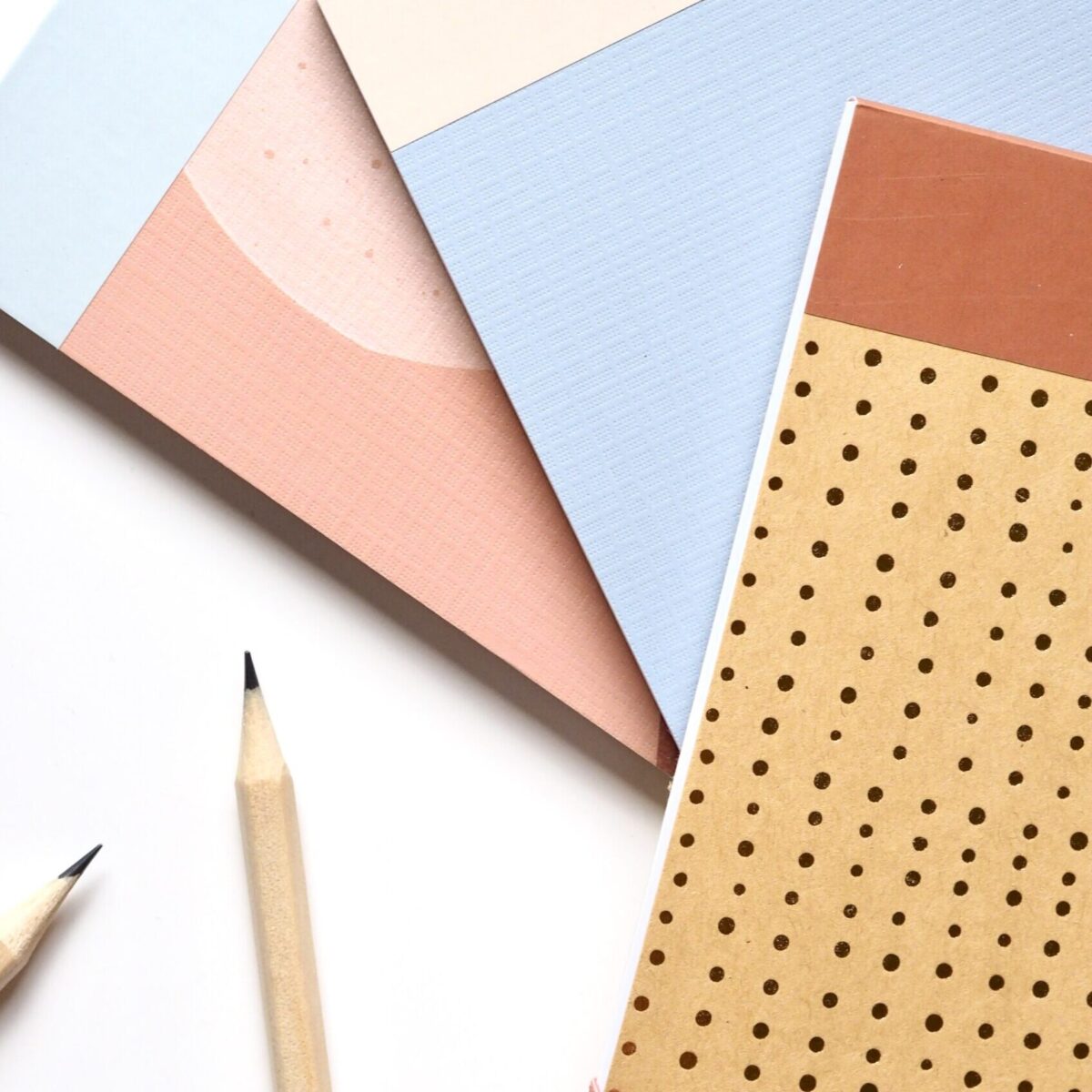 Two pencils placed next to a dotted journal with a colorful pastel background