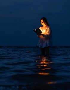 Illustration of a woman standing in dark water at night, reading a glowing book